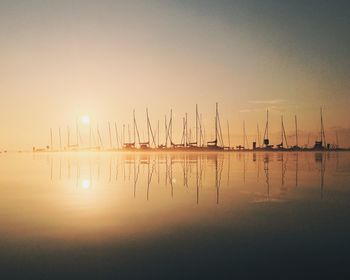 Sailboats moored on sea against sky during sunset