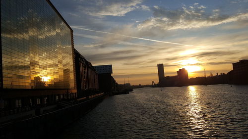 Bridge over river by buildings against sky during sunset