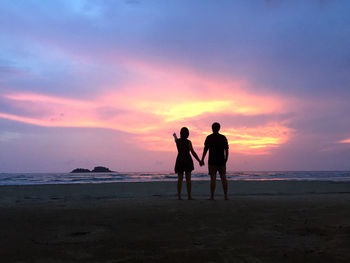 Silhouette friends on beach against sky during sunset