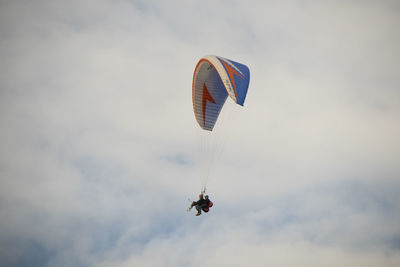 Low angle view of people paragliding against sky