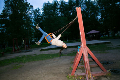 Beautiful young girl energetically and with pleasure swings on the swing at dusk.