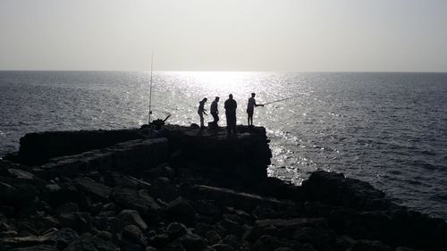 Silhouette people fishing in sea against sky