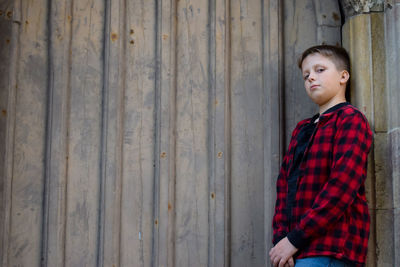 Portrait of boy standing against wooden wall