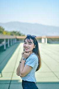 Portrait of smiling young woman standing at building terrace against sky