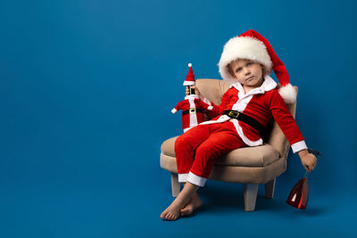Full length of young man sitting against blue background