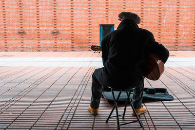 Rear view of woman sitting on brick wall
