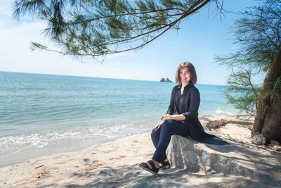 Young woman sitting on shore at beach against sky