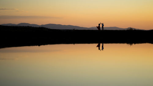 Silhouette people standing by lake against sky during sunset