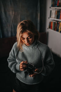 Woman holding camera while standing at home