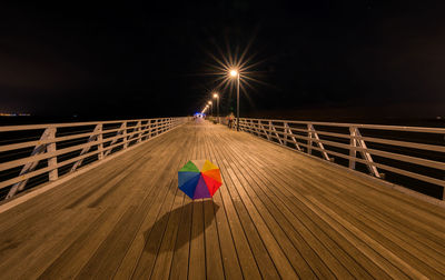 Light trails on footbridge against sky at night