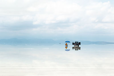 People by off-road vehicle on water at salar de uyuni against cloudy sky