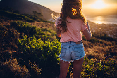 Rear view of woman standing on field against sky during sunset