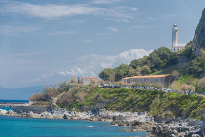 Lighthouse amidst sea and buildings against sky