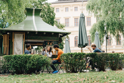 Smiling friends sitting at concession stand by plants in city