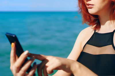 Midsection of woman using mobile phone in sea