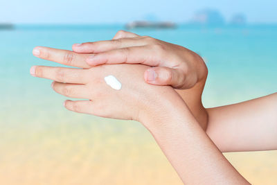 Close-up of hand holding hands over sea against sky