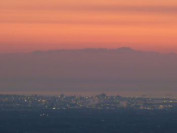 Illuminated cityscape against mountain during sunset