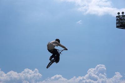 Low angle view of man with bicycle performing stunt against sky during sunny day