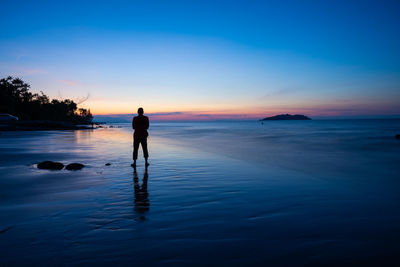 Rear view of silhouette man standing at beach against sky during sunset