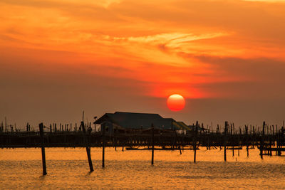 Silhouette wooden posts in sea against orange sky