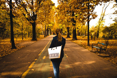 Rear view of woman walking on road amidst trees