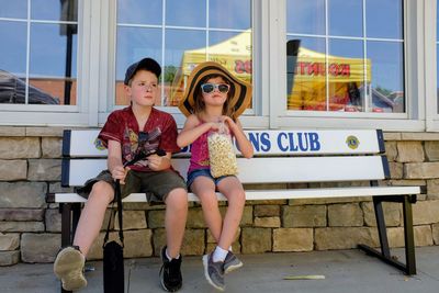 Girl having popcorn with brother while sitting on bench in city