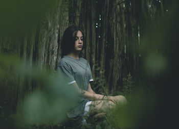 Young woman sitting by tree in forest