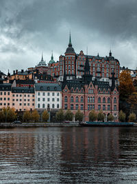 Buildings at waterfront against cloudy sky