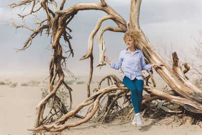 Mid adult woman sitting on tree at desert against sky