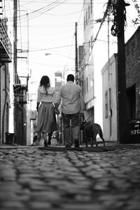 Rear view of people walking with dog on street in city