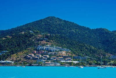 Buildings by sea against clear blue sky