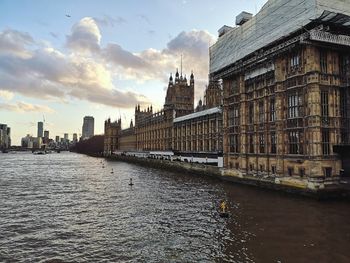 View of buildings by river against cloudy sky