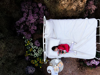 Drone shot of girl lying on bed amidst trees in forest