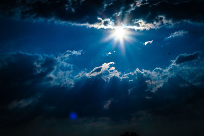 Low angle view of sunlight streaming through clouds