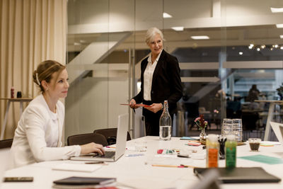 Mature professional discussing strategy while female colleague using laptop in global business meeting