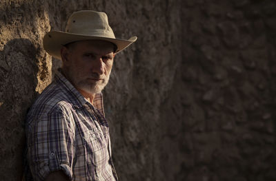 Portrait of adult man in cowboy hat and shirt against abandoned building