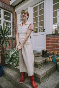 Mid adult woman holding kale leaf while standing in back yard