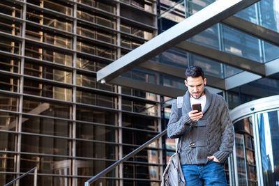 Man using smartphone outdoors, standing next to office building