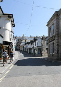 People walking on road amidst buildings in city against sky