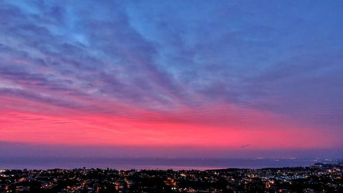 Illuminated cityscape against dramatic sky during sunset