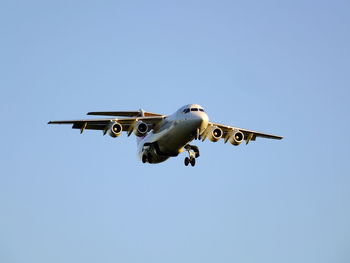 Low angle view of airplane flying against clear blue sky