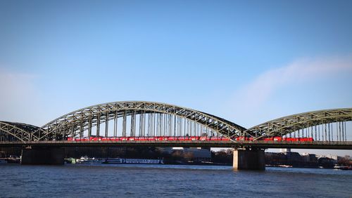 Red train on hohenzollern bridge over rhine against blue sky