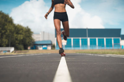 Low section of woman running on road against sky