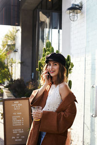 Young woman wearing sunglasses standing against glass wall