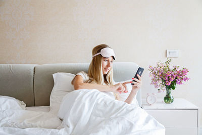 Young woman using smart phone while relaxing on bed at home