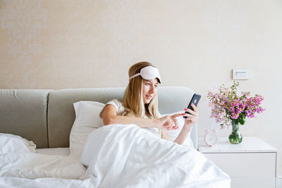 Young woman using smart phone while relaxing on bed at home