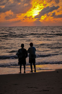 Men standing on beach against sky during sunset