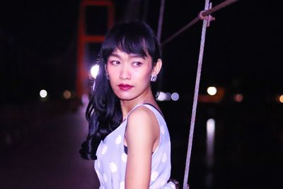 Side view of thoughtful young woman standing against bridge during night