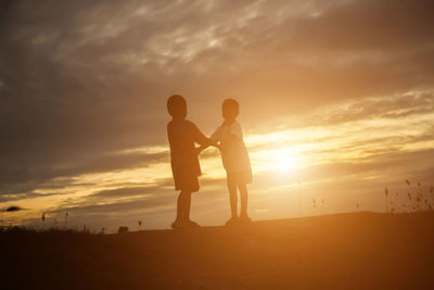 Silhouette friends standing on land against sky during sunset