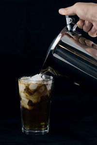 Cropped hand pouring drink in glass against black background